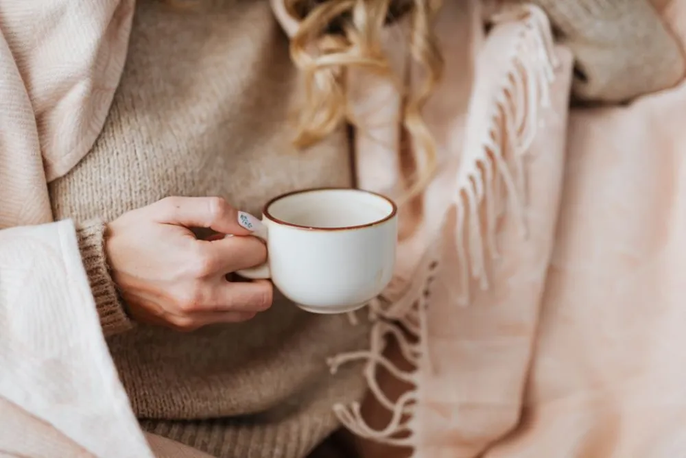 Close-up of a woman holding a coffee cup, wrapped in a cozy blanket.