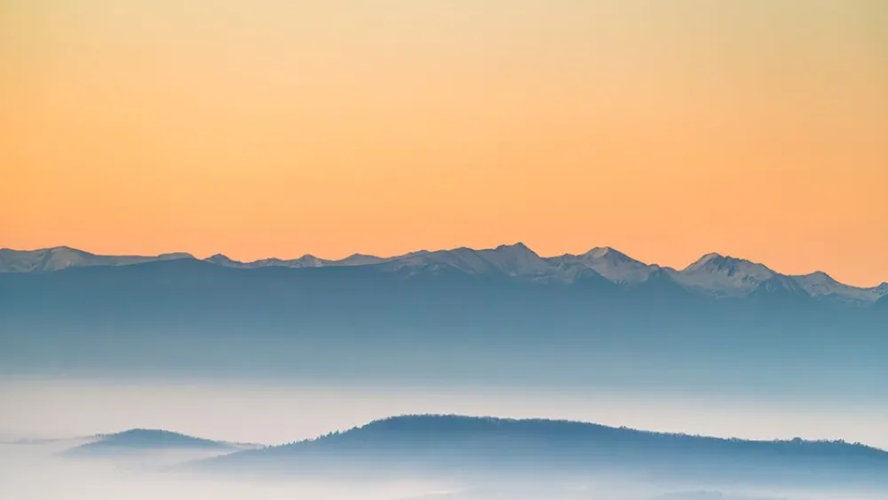 A peaceful view of misty mountains during sunrise with soft pastel colors.