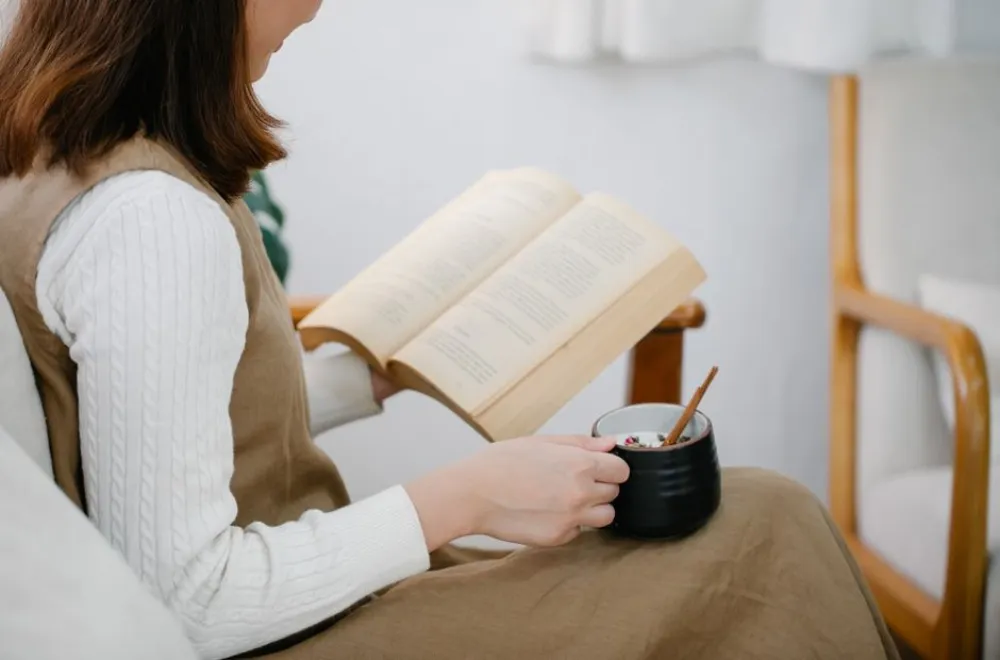 Женщина в кресле читает книгу и пьет чай в спокойной обстановке.