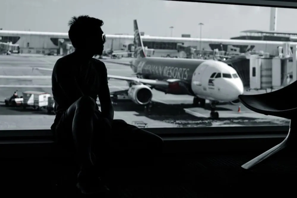 A silhouetted man sits in an airport terminal, viewing an airplane on the tarmac.