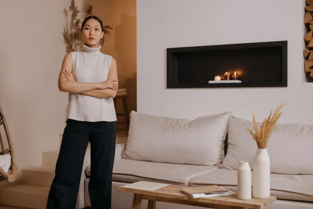 A woman stands in a stylish, minimalist living room with a cozy ambiance.