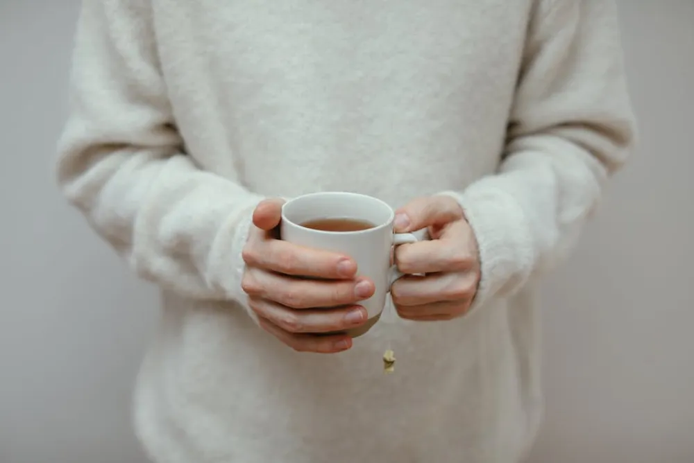 A close-up view of hands holding a hot cup of tea, dressed in a warm sweater.