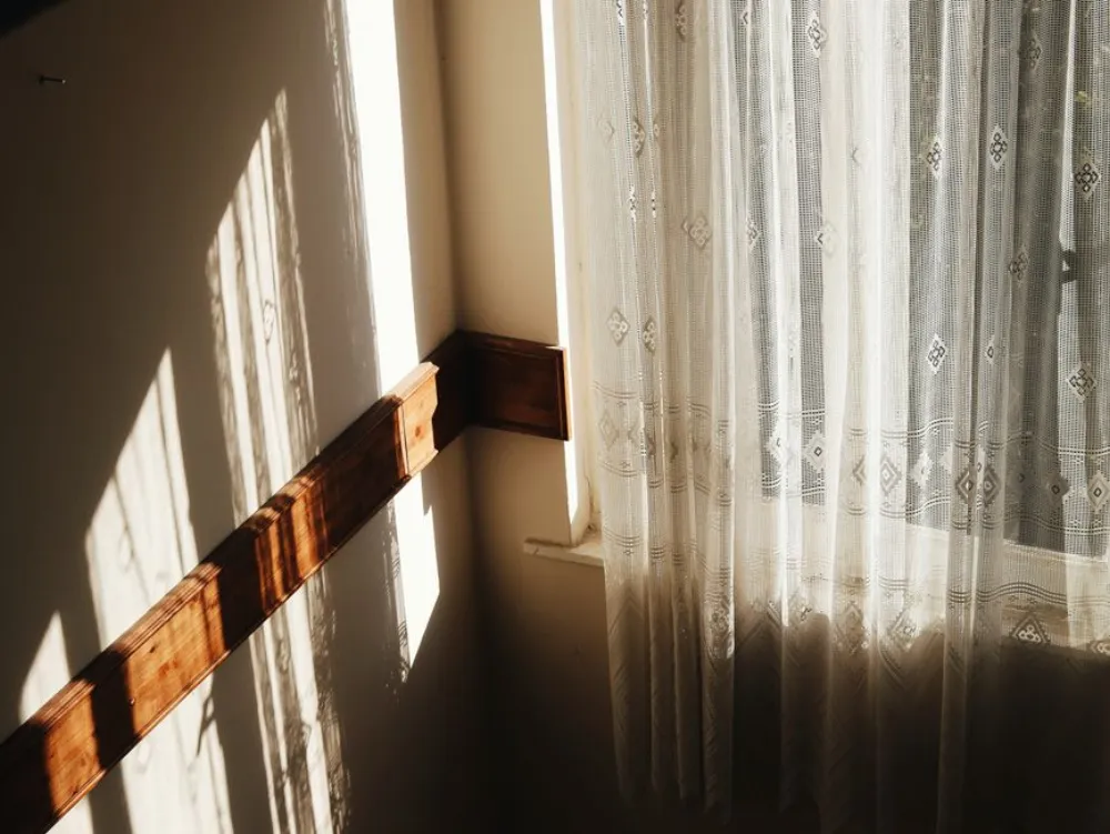 Tranquil scene of sunlight casting soft shadows through a lace curtain in a cozy room corner.